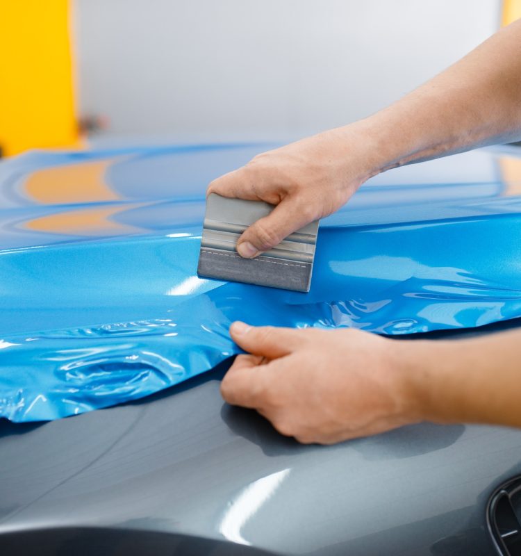 Car wrapping, mechanic with squeegee installs film